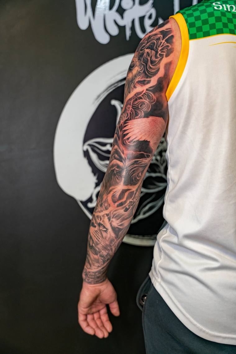 Finished blackwork sleeve on a man's left arm featuring a hannya mask near the wrist, flames, and a bird with outstretched wi