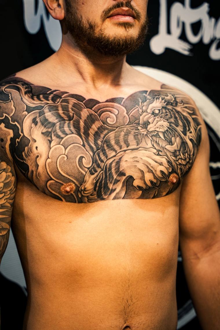 Finished Japanese irezumi tiger chest tattoo rendered in black ink with snarling feline, fangs, and swirling cloud motifs acr