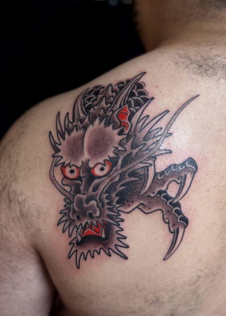 Freshly inked neo-traditional Japanese dragon head tattoo on shoulder, with snarling red eyes, bared fangs and a clawed talon