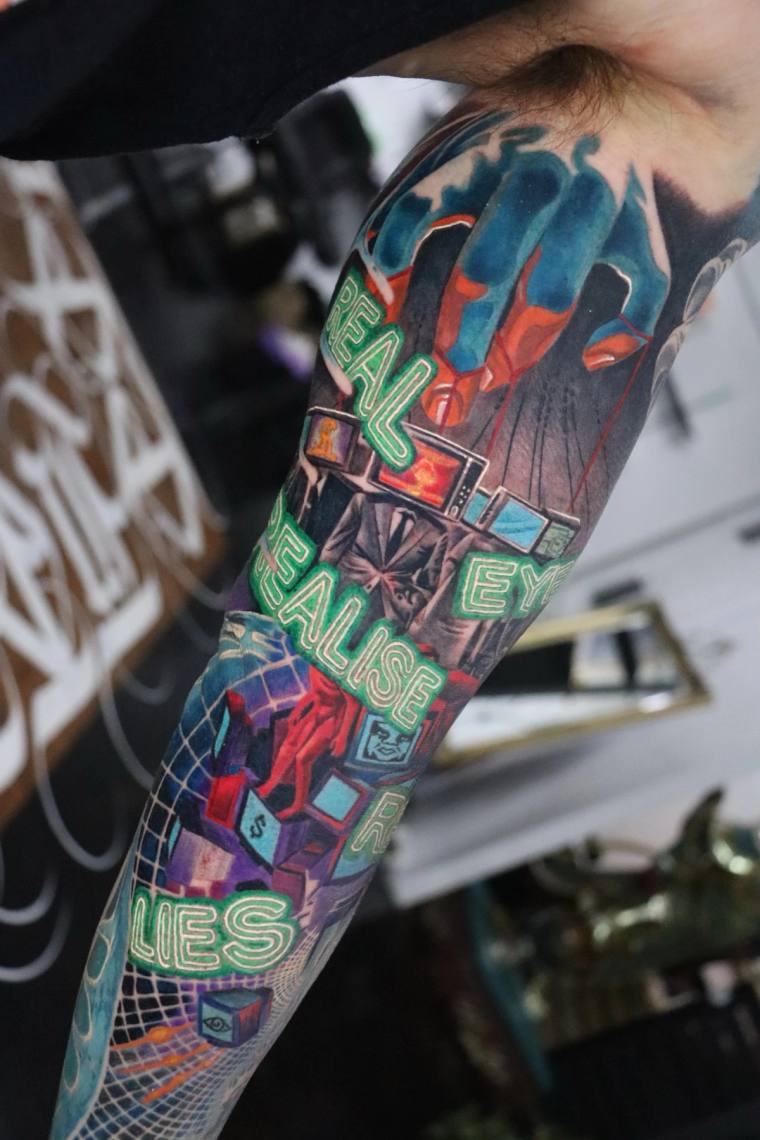 Colourful neo-traditional sleeve tattoo on a forearm featuring glowing green neon text reading 'EYE EYES REALISE' alongside r