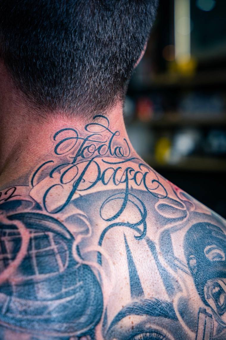 Back view of a person displaying a finished black and grey back tattoo with cursive 'Força' script on the neck, a globe, and 