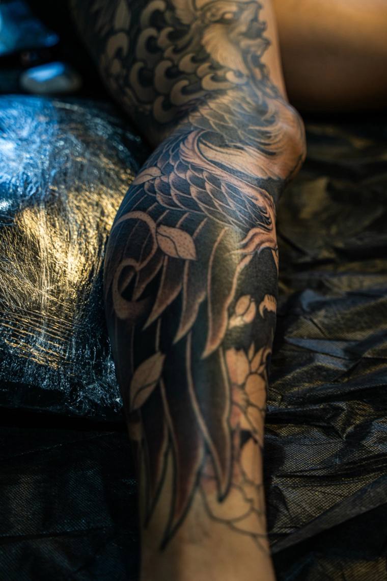 Black and grey irezumi forearm tattoo featuring a koi fish swimming through traditional Japanese waves and clouds, with a chr