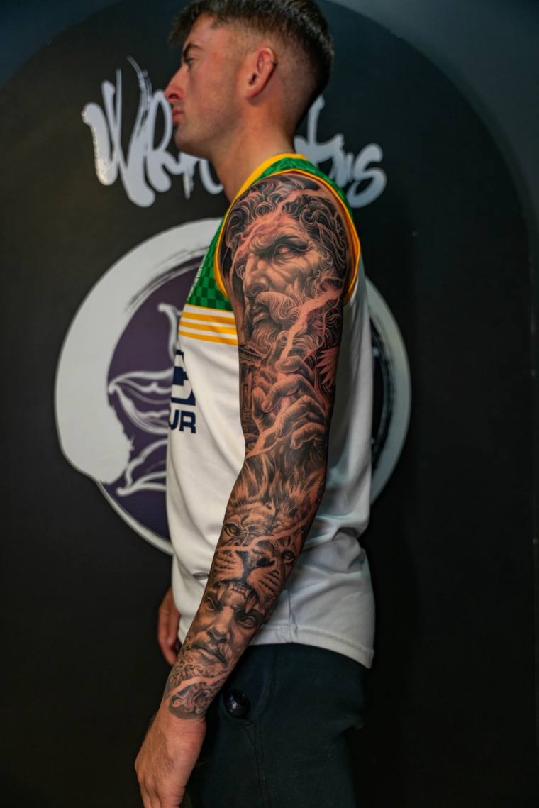 Finished blackwork sleeve on a man's right arm featuring a bearded Greek deity wielding lightning bolts on the upper arm and 