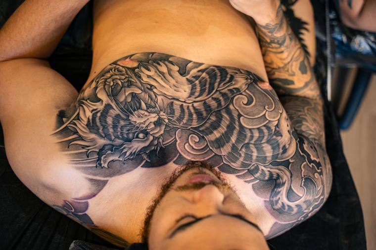 Large finished Japanese-style irezumi blackwork tattoo of a tiger emerging from clouds and waves across a man's chest.