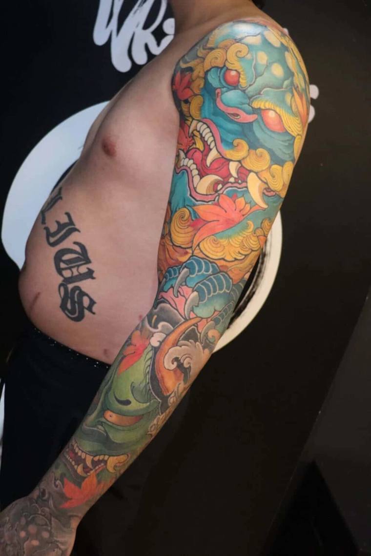 Colorful irezumi full sleeve featuring a foo dog shisa with clouds and peonies, plus kanji on the ribs.