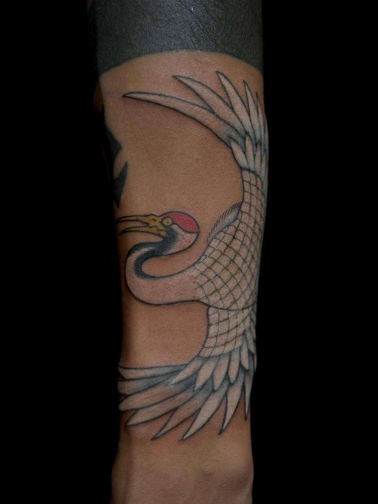 Traditional Japanese irezumi crane tattoo in flight on a forearm, with detailed black and grey feather work, red crown, and y