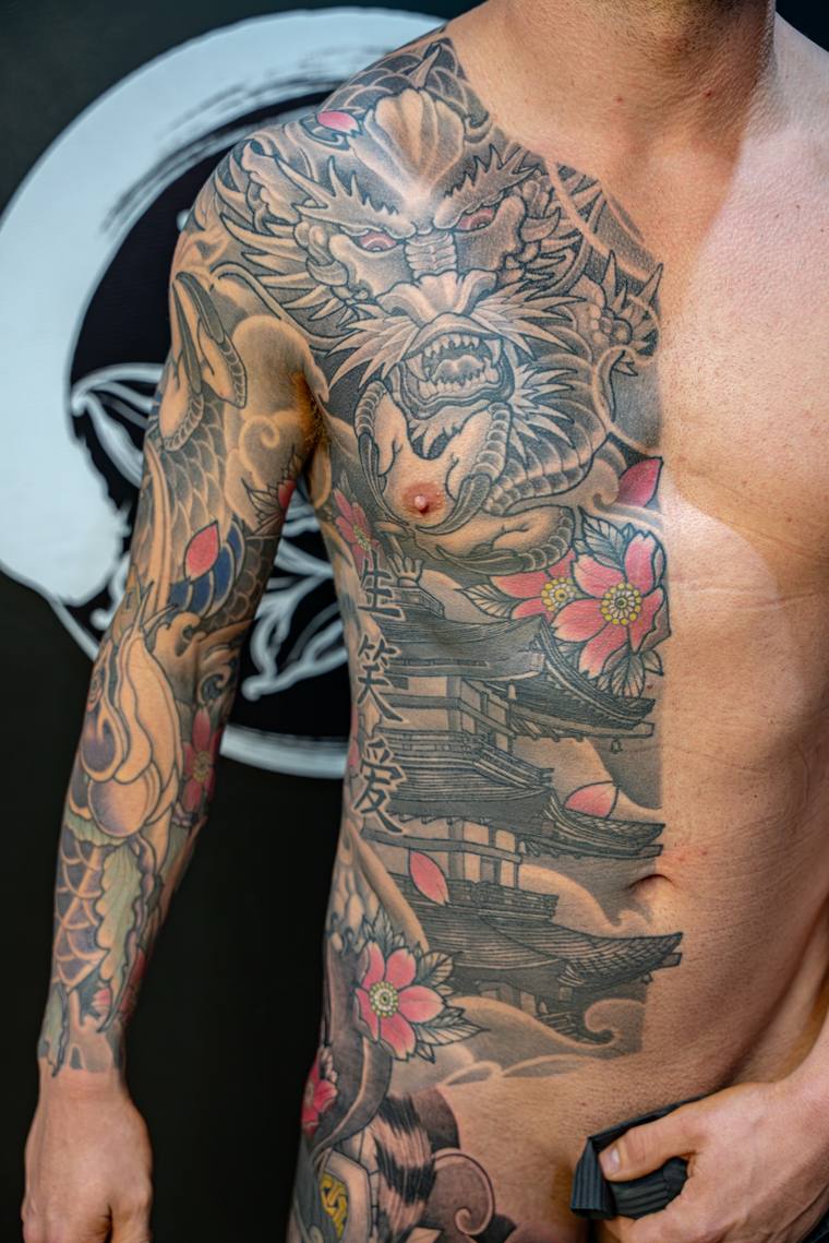 Finished irezumi half-sleeve and chest piece featuring a snarling dragon, cherry blossoms, a pagoda, kanji, and clouds in bla