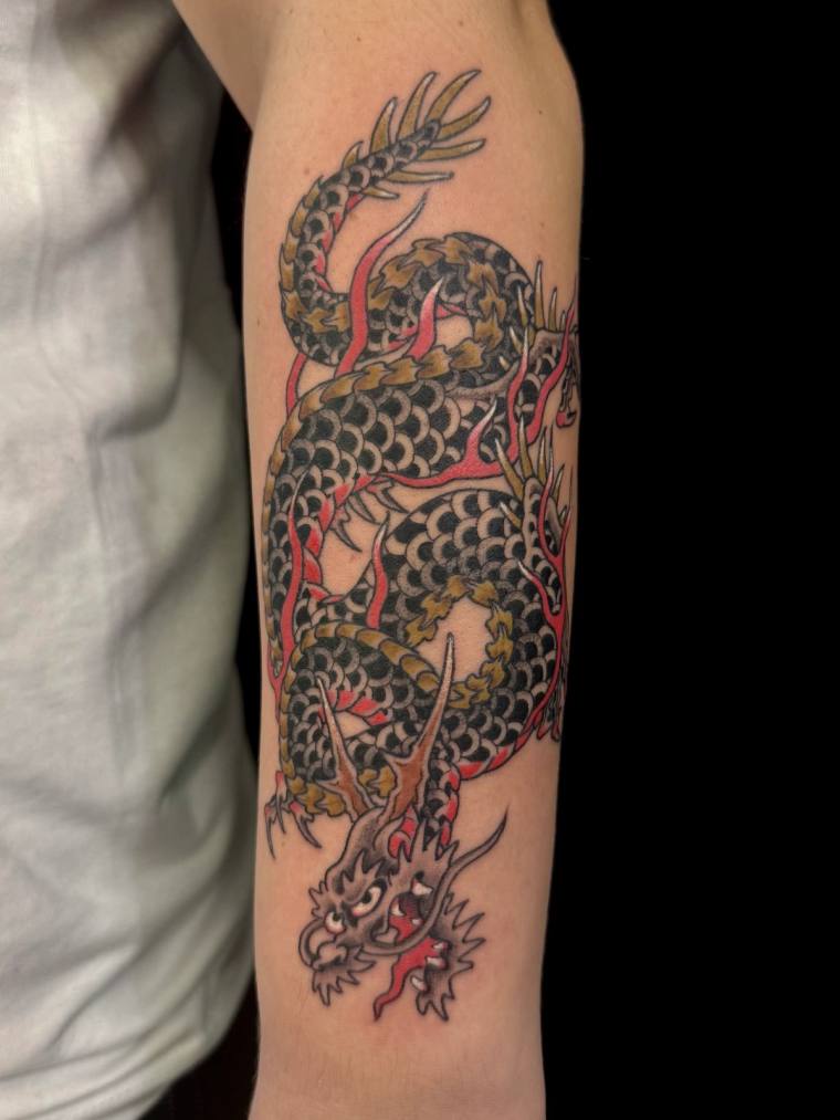 Finished Japanese-style dragon tattoo on a forearm, featuring black scales, golden-yellow highlights, and red flames coiling 