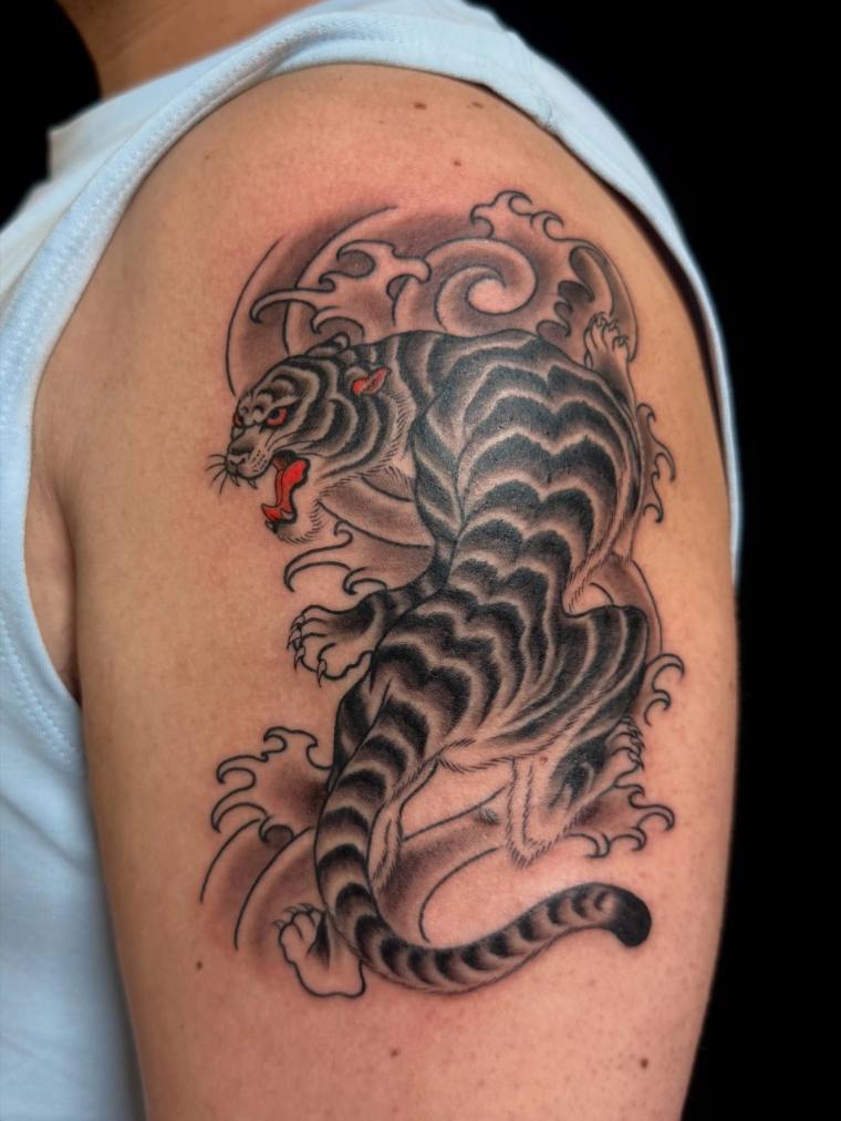 Traditional Japanese irezumi tattoo of a snarling tiger with red eyes and mouth, surrounded by stylized waves and clouds on a