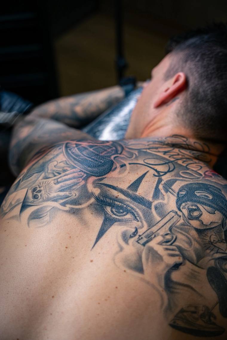 Healed black and grey back tattoo featuring a central all-seeing eye with starburst, a hand holding a globe, a hand gripping 