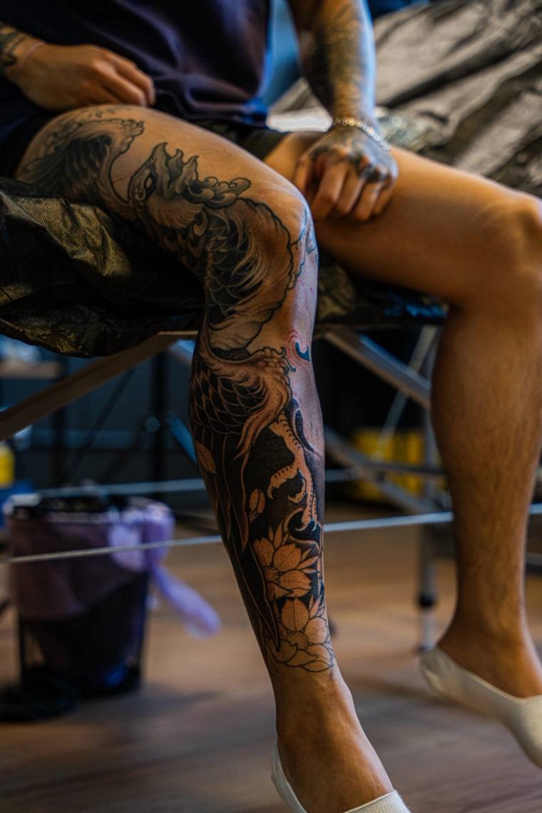 A large irezumi leg sleeve featuring a koi fish, dragon, flowing waves and lotus flowers in black and grey ink.