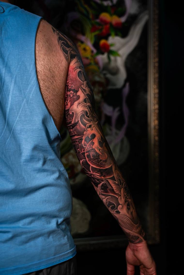 Finished irezumi full sleeve tattoo on a man's left arm featuring a dragon, pagoda, and ocean waves in black and grey with re