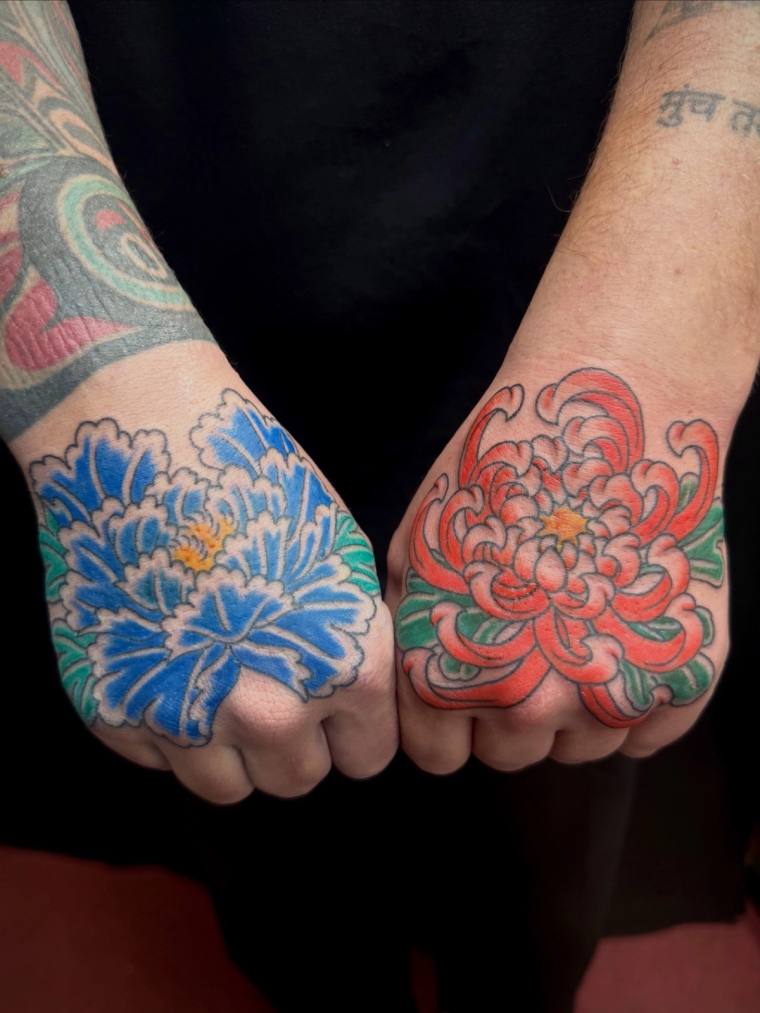 Two clenched fists displaying matching Japanese-style chrysanthemum tattoos: a blue kiku on the left hand and a red-orange ki