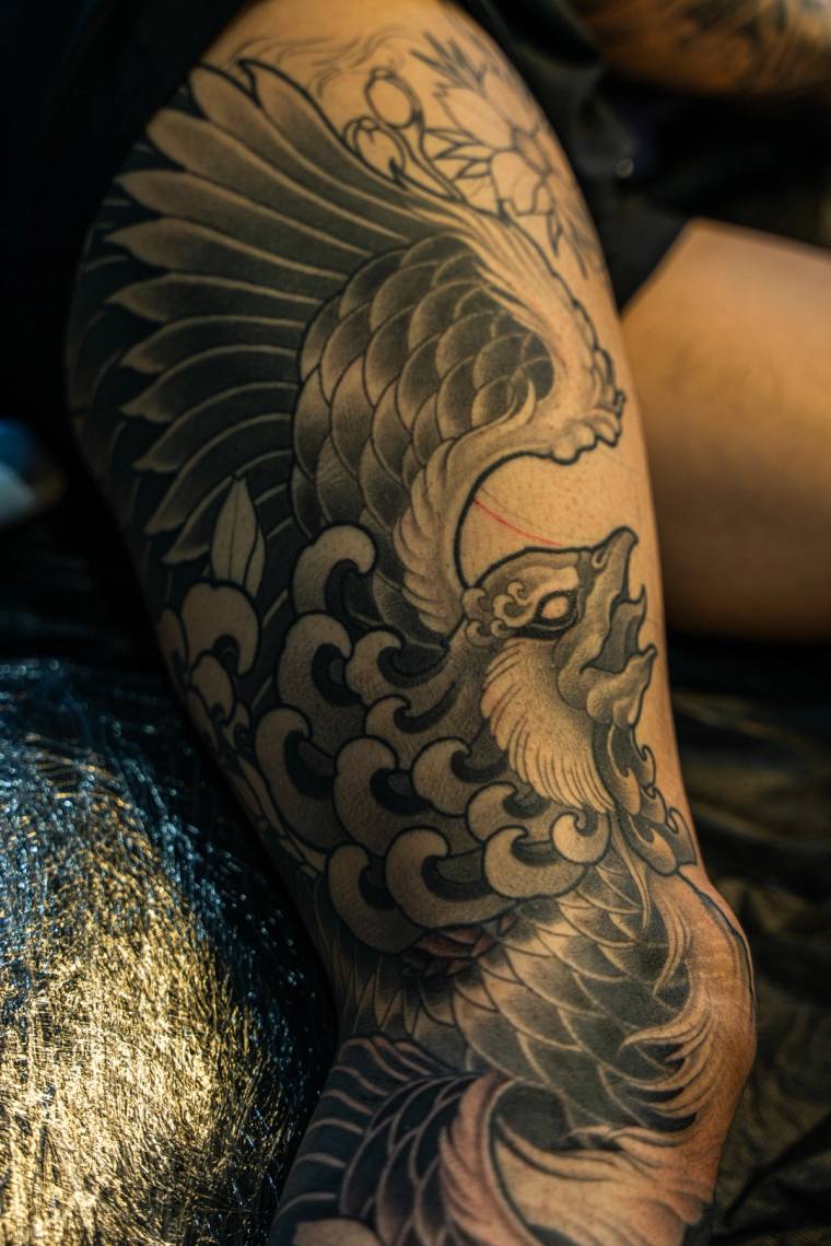 Finished black and grey irezumi sleeve featuring a koi fish swimming through traditional Japanese waves and clouds with flowe