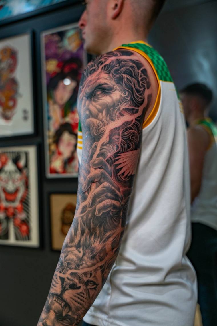 Finished black-and-grey full sleeve tattoo on a man's right arm, featuring a bearded deity, praying hands, and a cat face.