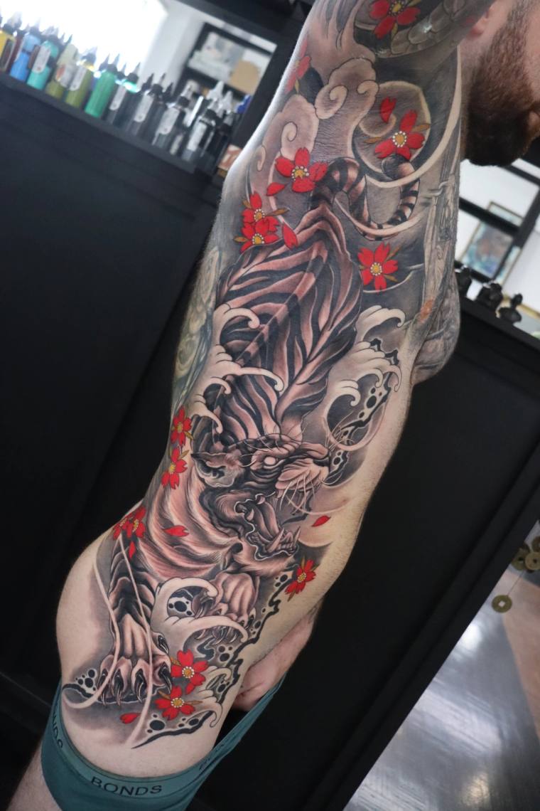 Japanese irezumi full sleeve tattoo featuring a snarling tiger surrounded by red cherry blossoms, crashing waves and traditio