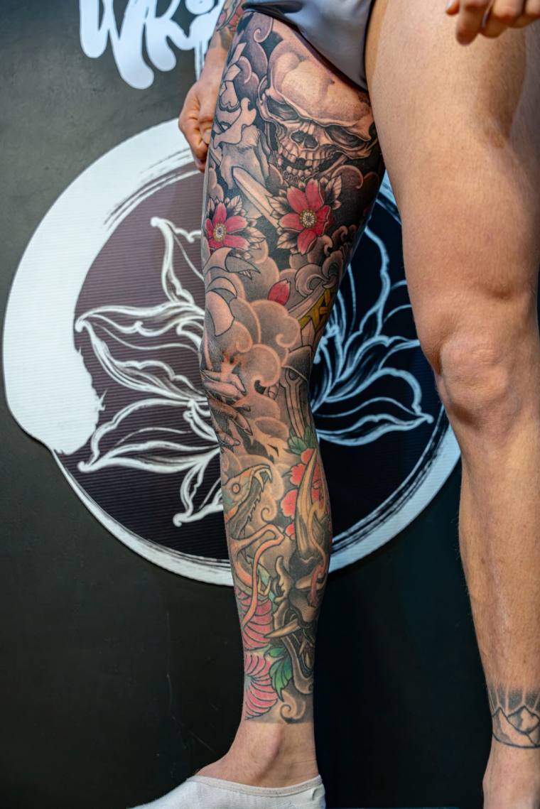 Finished full-leg irezumi sleeve featuring a skull, red peonies, a dragon, koi, and swirling clouds on a model's leg.
