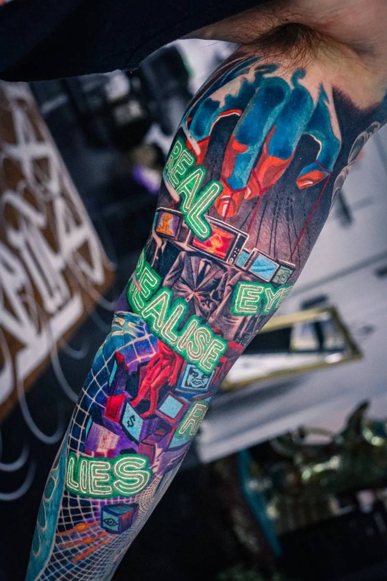 Full sleeve tattoo on forearm featuring neon green stylized text reading EYES FALISE EYES LIES, retro TV sets, a red figure, 
