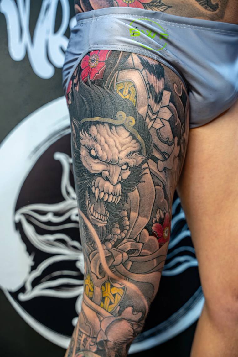 Irezumi thigh tattoo of a snarling demon warrior in a kabuto helmet, with bared fangs, wild hair, red cherry blossoms, and go