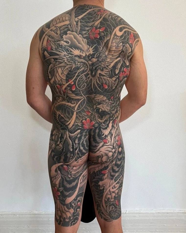 Large irezumi back tattoo featuring an intertwined dragon and tiger with cherry blossoms and clouds, extending from shoulders