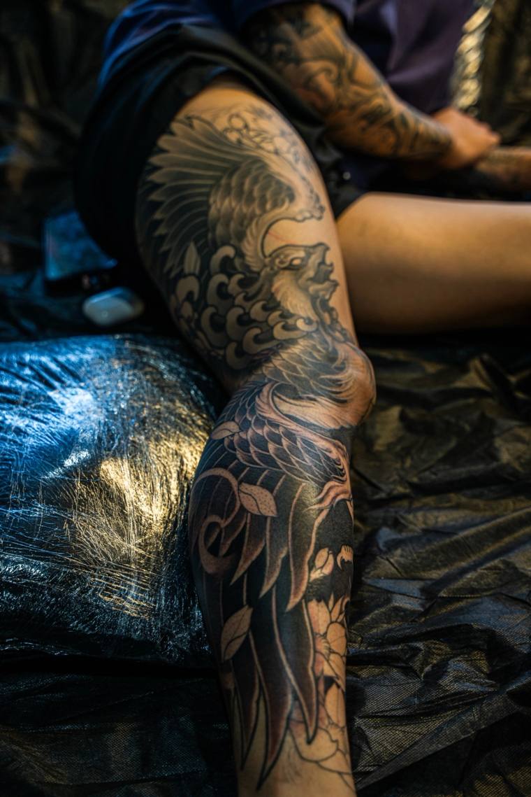 Finished black irezumi phoenix leg sleeve with detailed feathers, swirling clouds, and flowing leaves wrapping the thigh and 