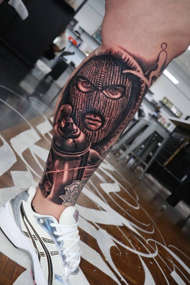 Finished blackwork samurai mask tattoo with flame details on a calf, photographed inside a studio with white athletic shoes v