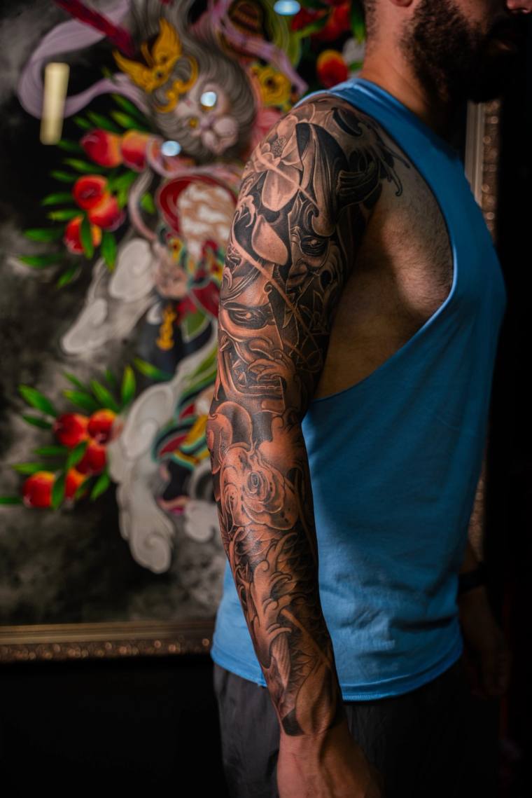 Finished black and grey irezumi full sleeve featuring a hannya mask, samurai figure, and floral motifs on a man's arm.