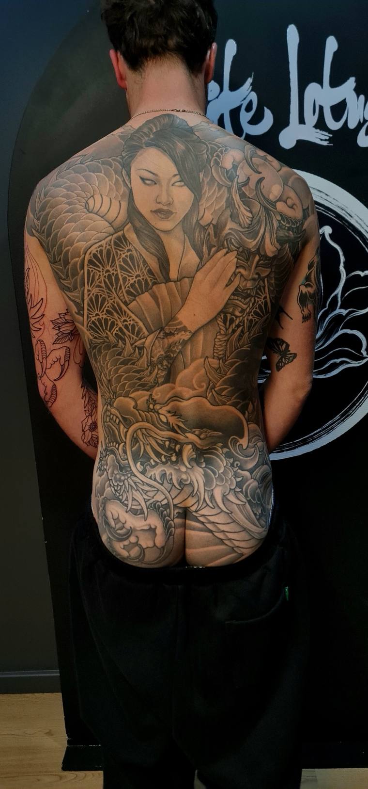 Finished full back irezumi tattoo of a geisha holding a fan, with a dragon, koi fish, waves, and cherry blossoms in black and