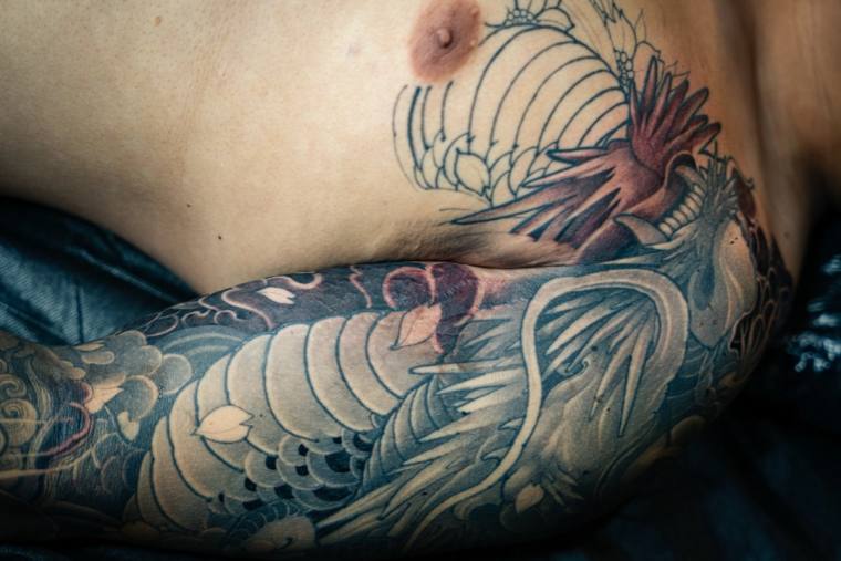 Large Japanese irezumi tattoo of a red and grey dragon with wind bars and clouds wrapping around a man's side torso and ribs.