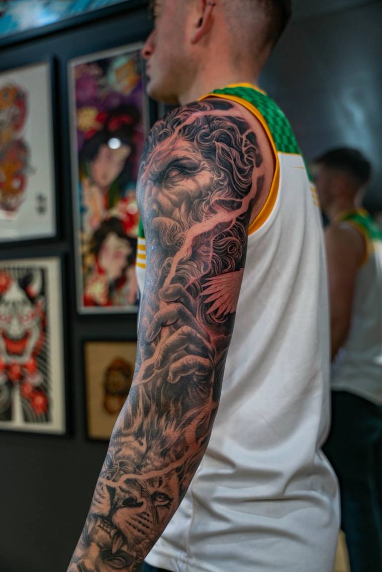 Side view of a man wearing a white tank top, displaying a finished irezumi sleeve with a bearded sage, dragon, and tiger in b