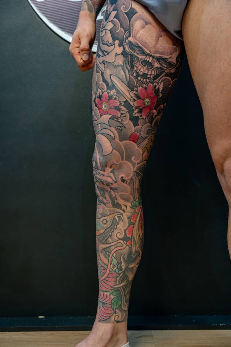 Finished irezumi full-leg sleeve featuring a skull, red cherry blossoms, clouds, a coiling snake, and a koi fish near the ank