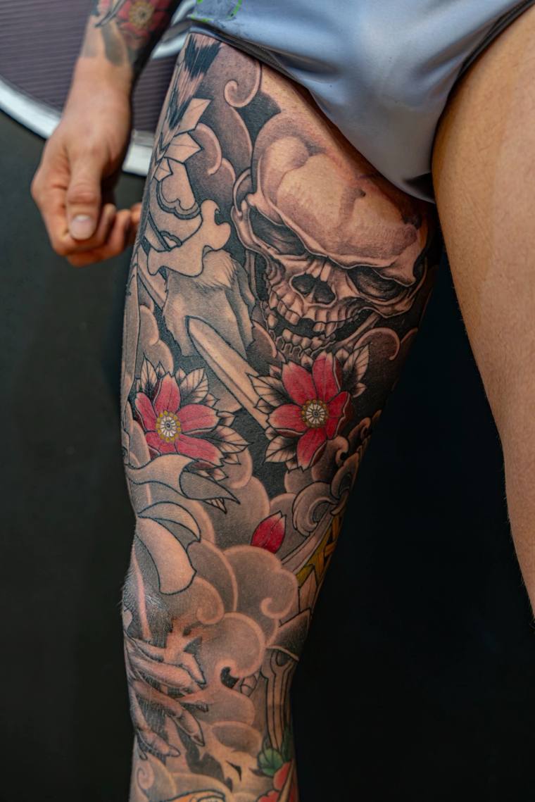 Finished irezumi thigh tattoo featuring a grinning skull surrounded by red cherry blossoms and traditional Japanese cloud mot