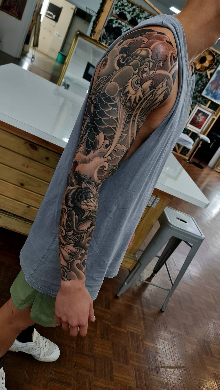 Finished black and grey irezumi sleeve on a man's left arm featuring a koi fish, hannya mask, and crashing waves inside a tat