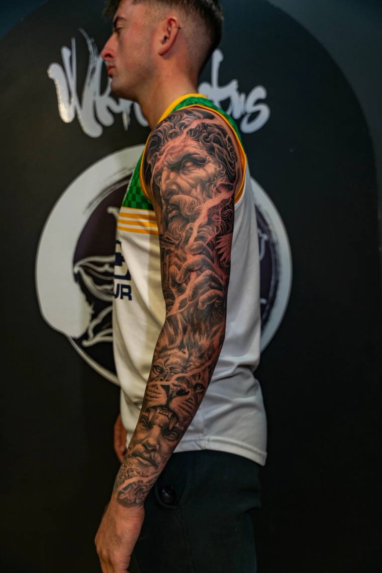 Finished black and grey realism sleeve featuring a Zeus-like bearded god, wolf, lion, and classical portrait on a man's right