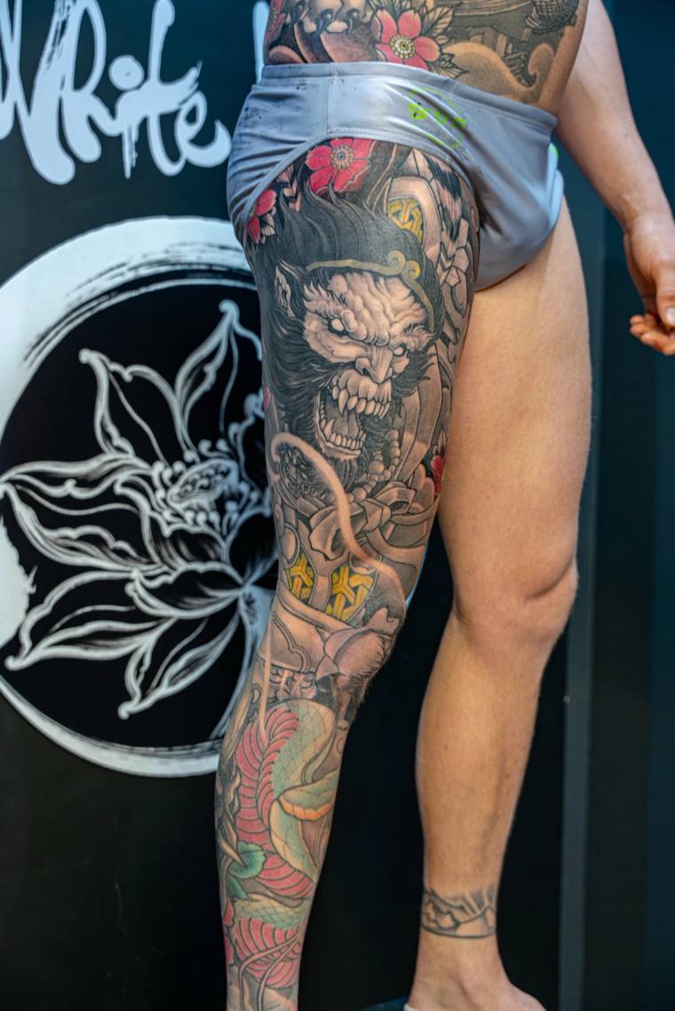 Full irezumi leg sleeve featuring a snarling oni demon face, cherry blossoms, skull, and lotus in vibrant colour.