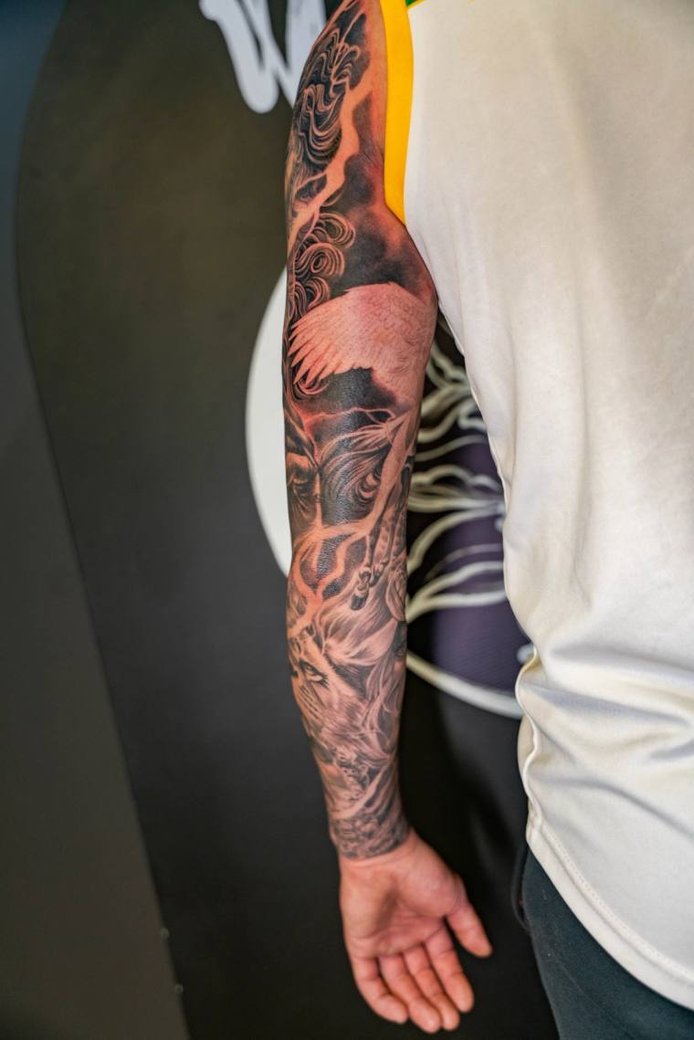 Black and grey irezumi full sleeve featuring a fox, crane, horned dragon, and swirling clouds on a man's arm.