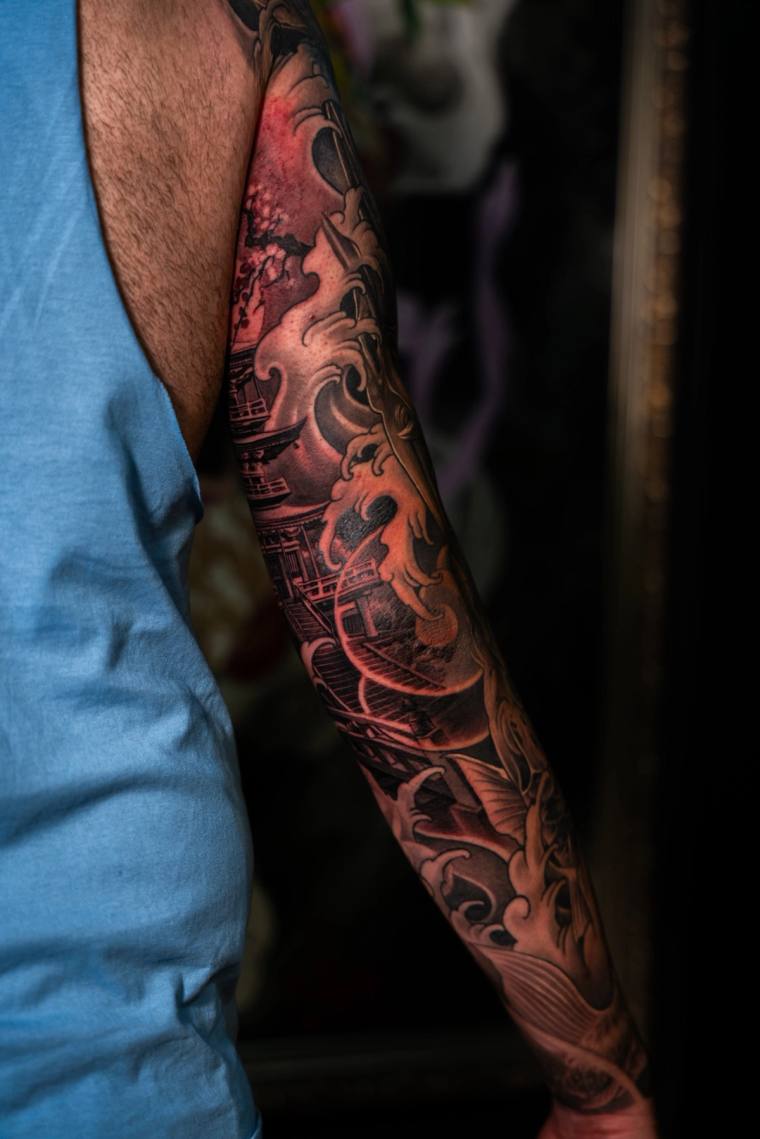 Japanese irezumi full sleeve tattoo on a man's arm showing a pagoda, swirling smoke and waves rendered in black and grey with