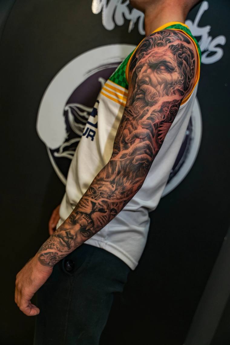 Finished black and grey full-sleeve tattoo featuring a bearded Greek god portrait at the shoulder, a hand, and a tiger face n