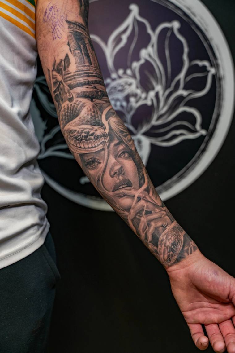 Finished greywash forearm tattoo featuring a realistic woman's face beneath a hooded cobra, with a tower in the background.