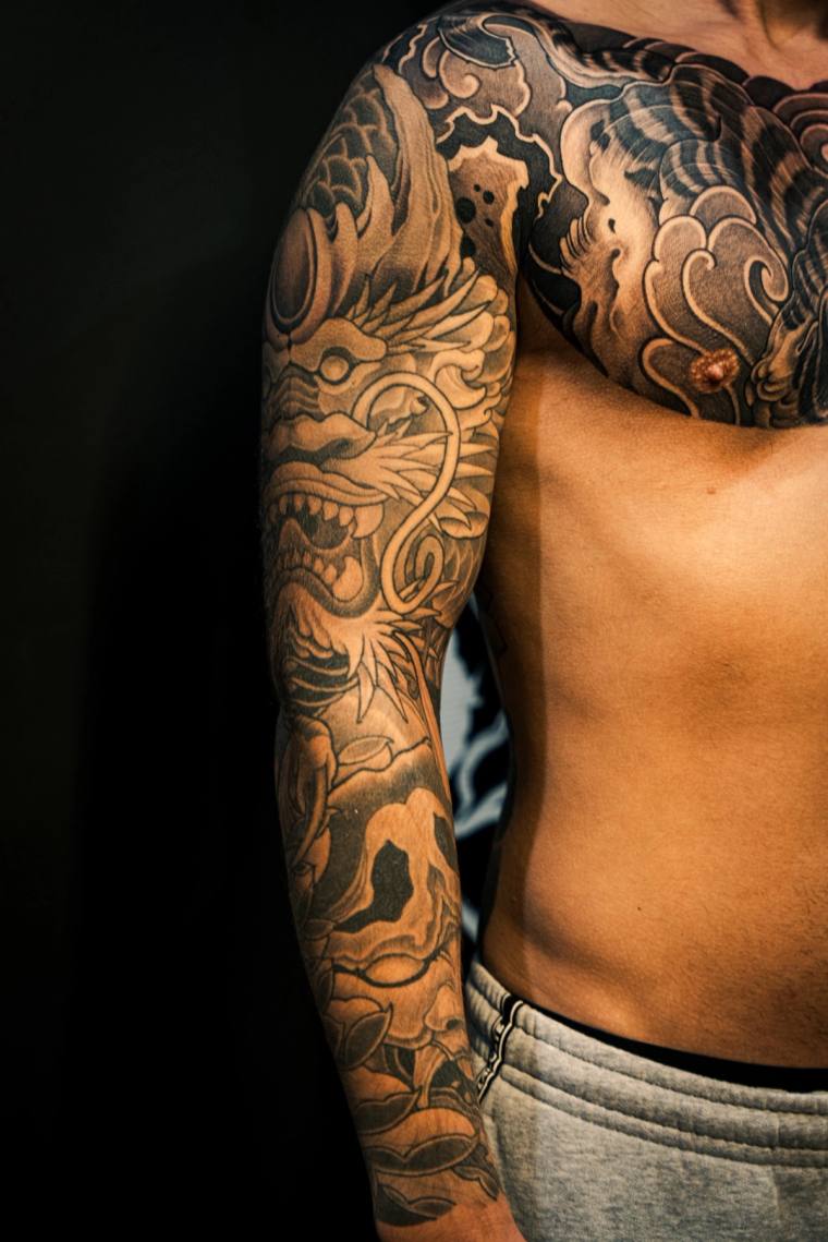 Finished blackwork irezumi sleeve and chest piece featuring a snarling shishi face on the shoulder, a skull on the forearm, a
