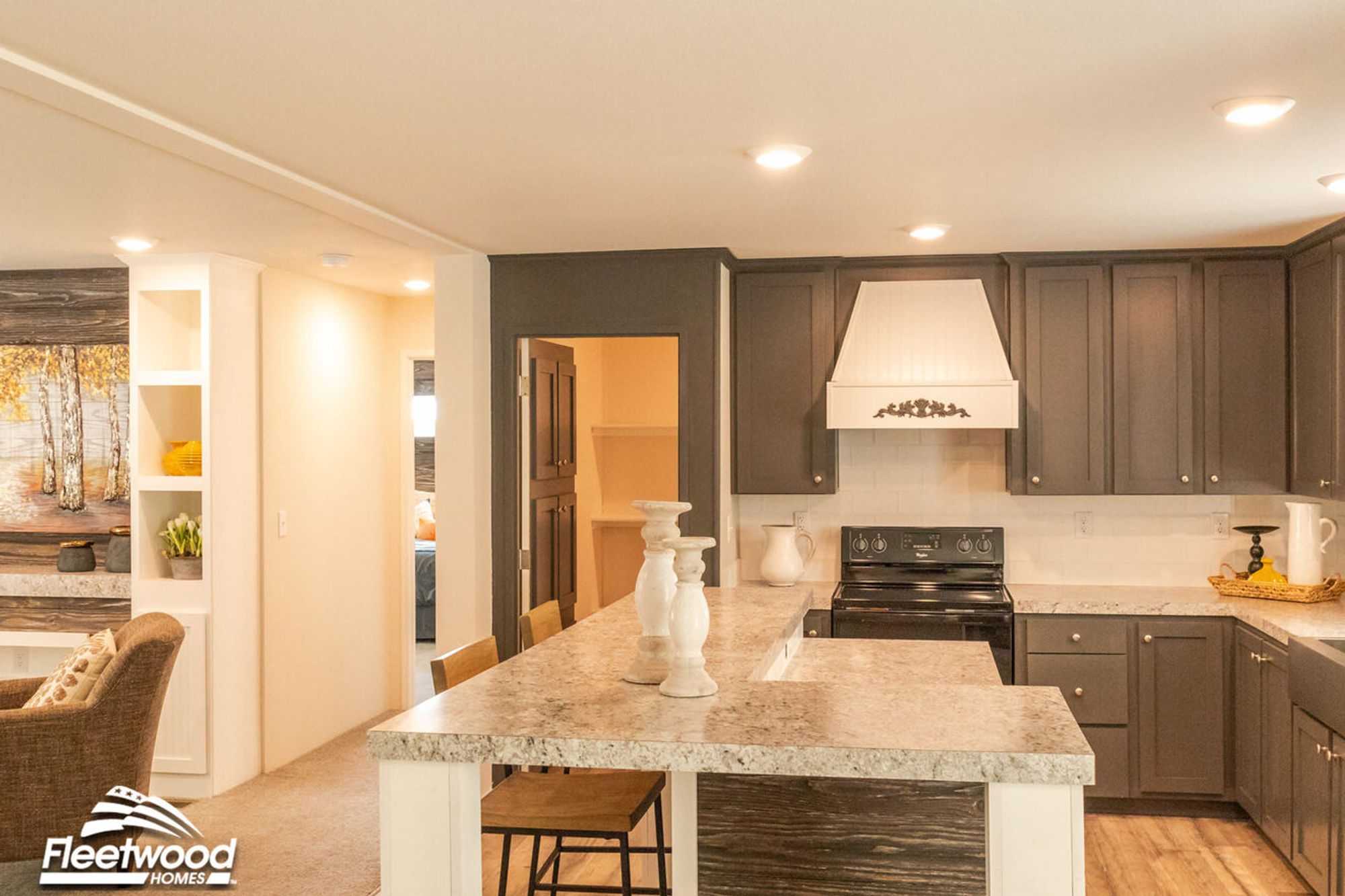 Warm kitchen with granite-style countertops, dark cabinetry, white range hood, black appliances, and a breakfast bar with white candle decor.
