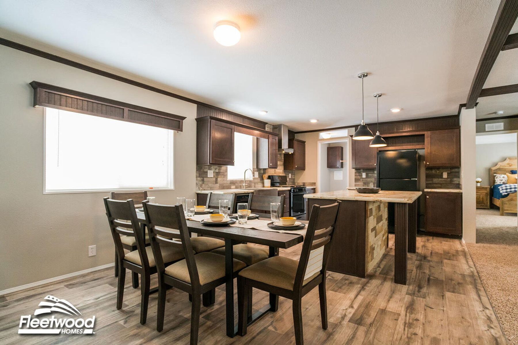 Open kitchen and dining area with a six-seat wooden dining table, dark wood cabinetry, kitchen island, and black appliances on wood-look flooring.