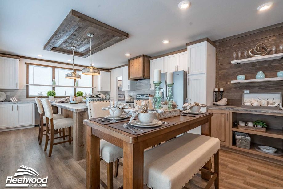 Bright kitchen and dining area with rustic wood accents, white cabinetry, stainless steel appliances, a wood island with pendant lights, and a wooden dining table set for four.