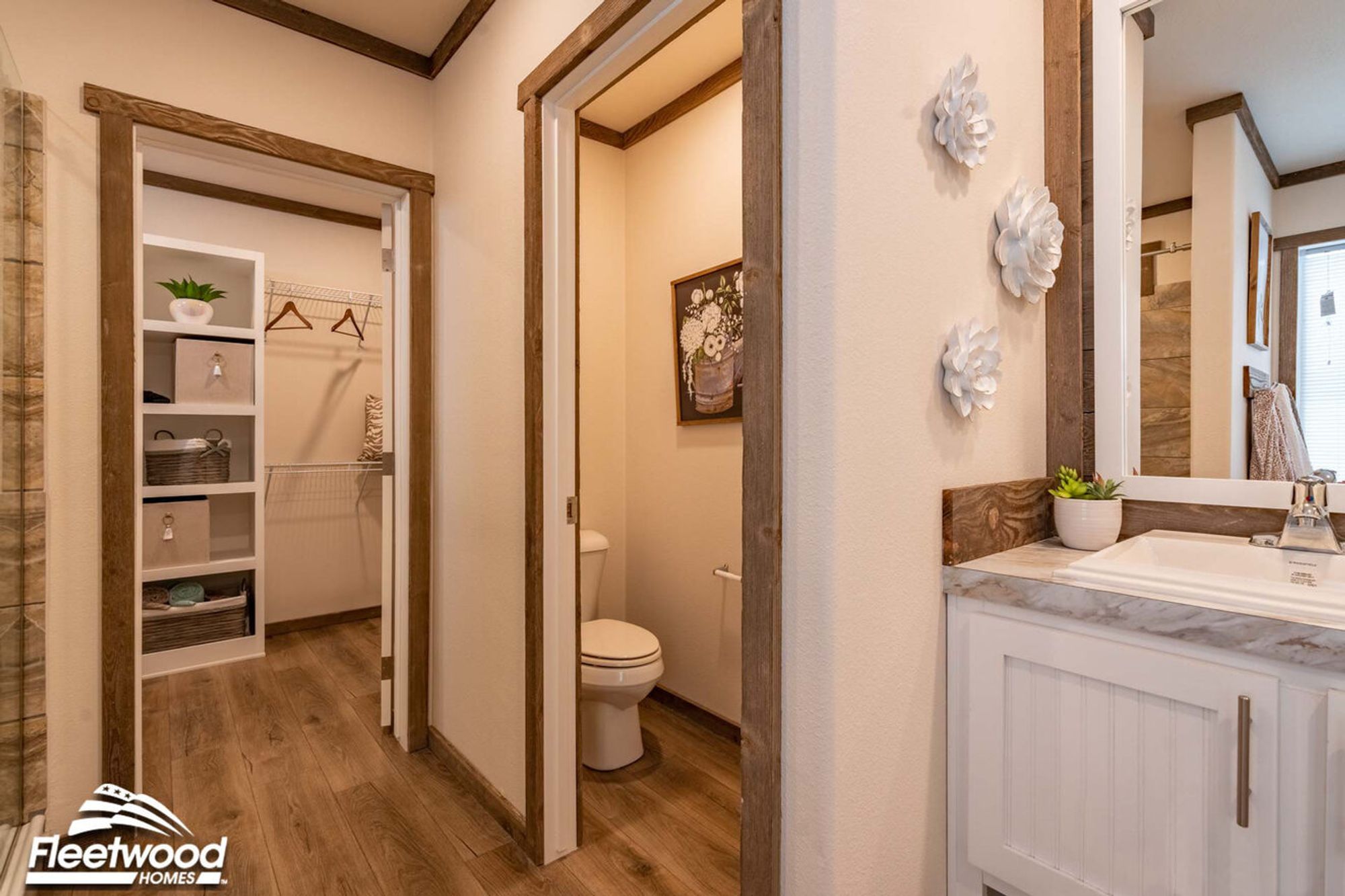 Bathroom with a vanity and marble-style countertop, a private toilet area, decorative wall accents, and a view into an adjacent walk-in closet with built-in shelving.