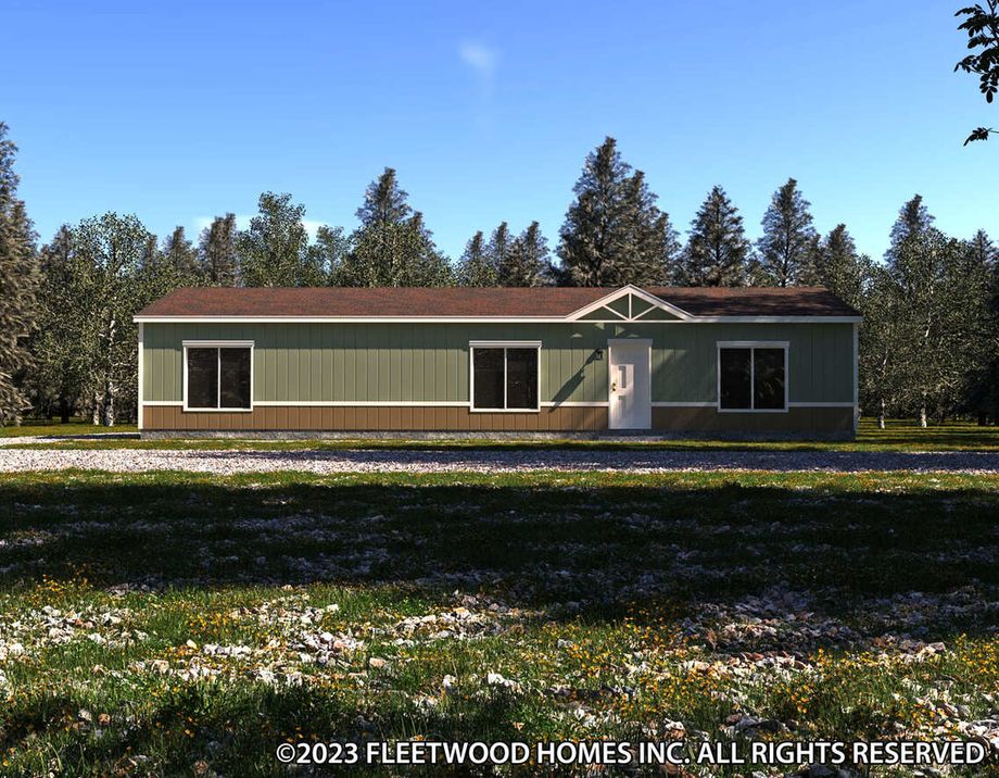 Single-story manufactured home with green and brown siding, white trim, a front entry door, and large windows, set against a wooded backdrop.