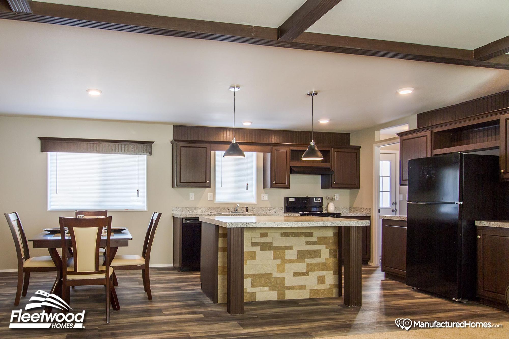 Open kitchen and dining area in a manufactured home, featuring dark wood cabinetry, granite countertops, a set dining table, and pendant lighting over the island.