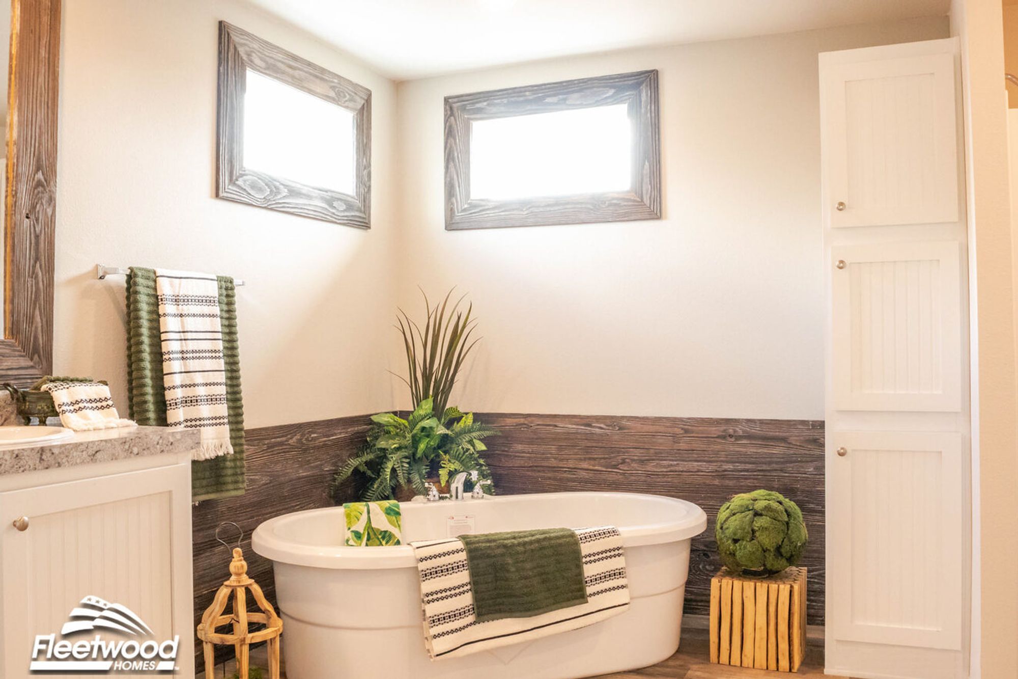 Spa-inspired bathroom with freestanding oval tub, wood-look wall paneling, greenery, and a mix of green and white towels and accents.