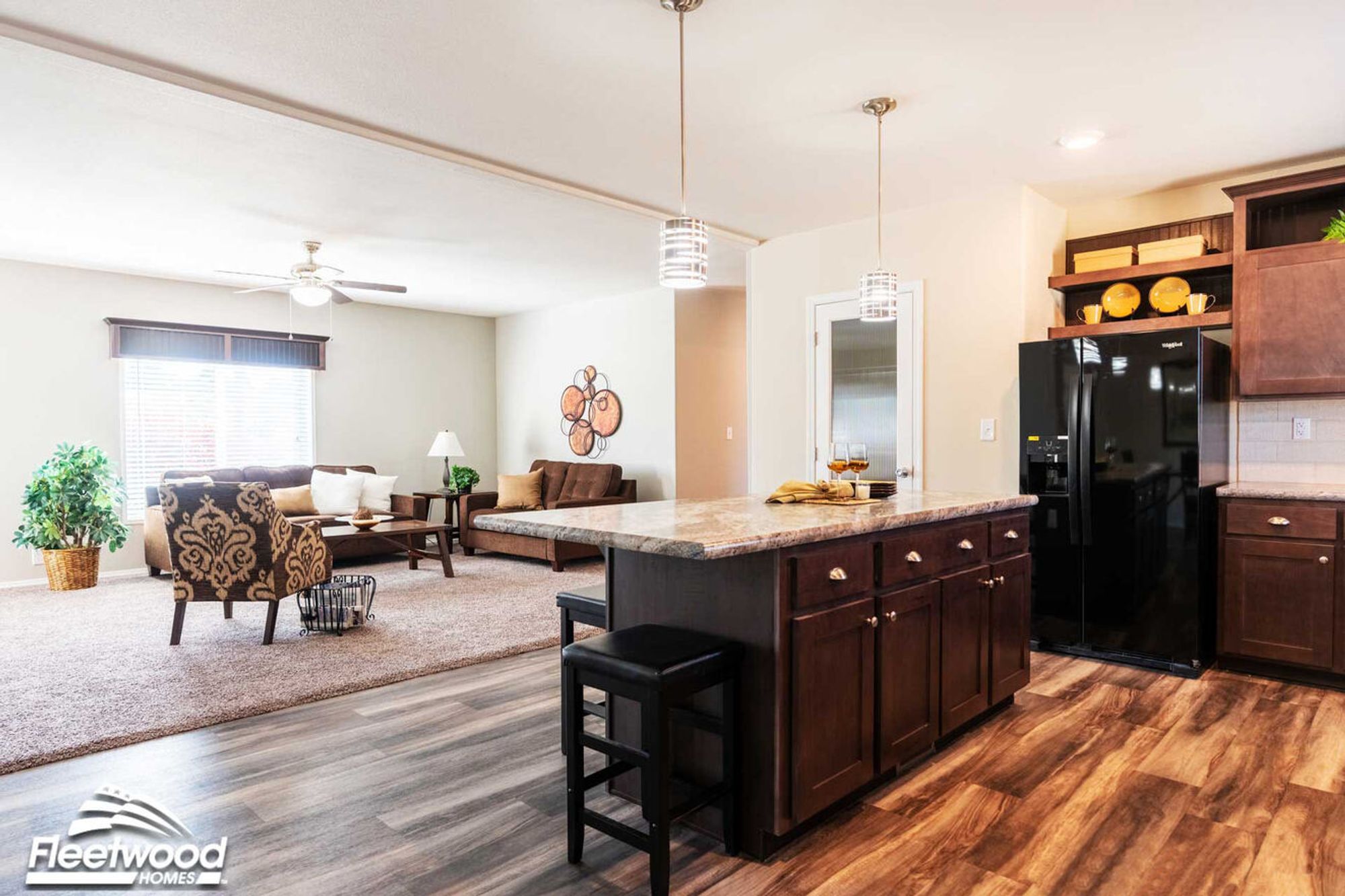 Open-concept dining, kitchen, and living area with dark wood cabinets, center island, modern lighting, and cozy seating by a large window.
