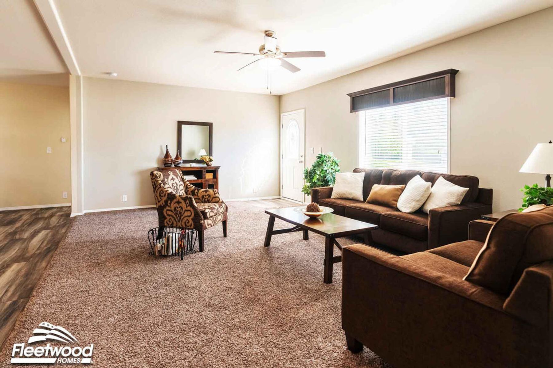 Cozy living room with brown sofas, accent chair, coffee table, and neutral decor, featuring carpet flooring and a ceiling fan.