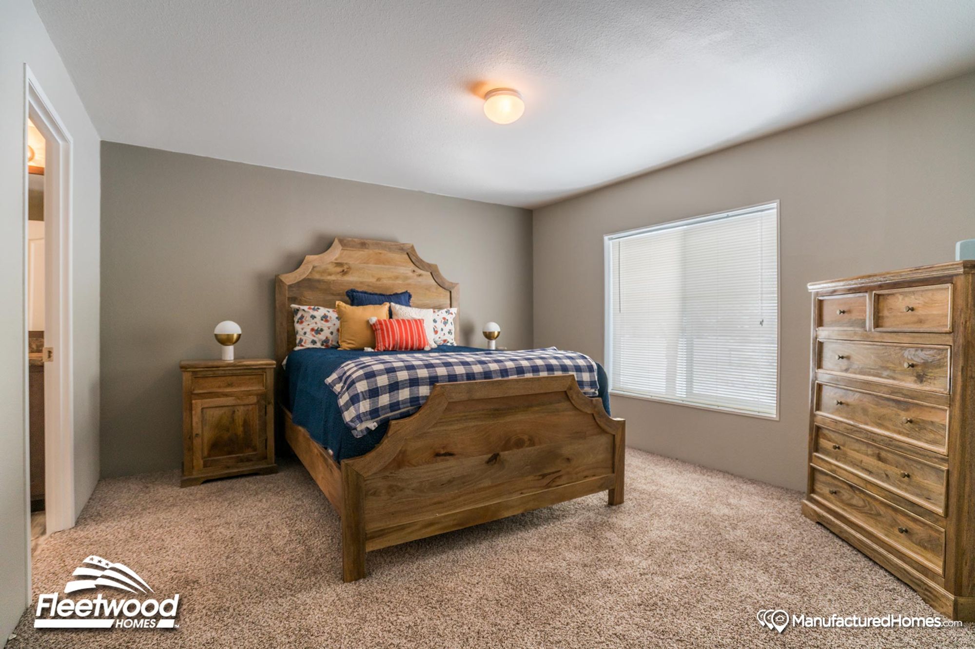 Bedroom with rustic wood furniture, including a sculpted headboard bed, matching nightstand and dresser, colorful throw pillows, and neutral-toned carpeting.